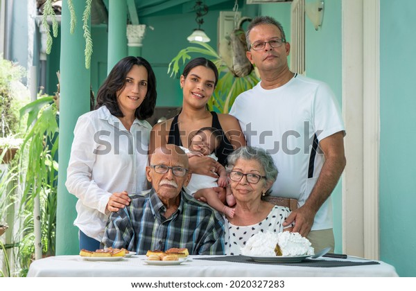Elderly\
couple sitting. A man a woman and a young woman with a child in\
their arms standing behind the elderly\
couple