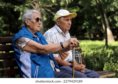 Elderly couple sitting on a bench in spring or summer park. Old man and woman outdoors, life in retirement - Powered by Shutterstock