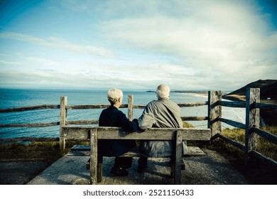 Elderly couple sitting on a bench, overlooking the ocean. The elderly couple enjoys the ocean view. The elderly couple, a man and woman, relax by the ocean. Sea view landscape with old man and woman. - Powered by Shutterstock