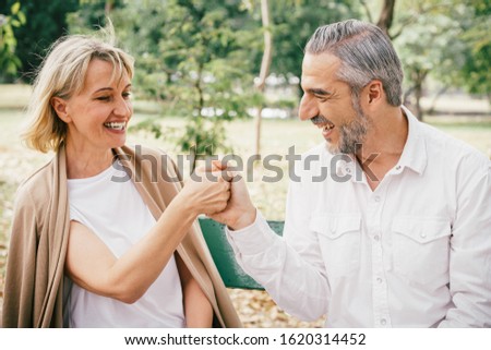 Elderly couple sitting on a bench tease each other having fun and laughing happily together at the public park in the morning. Happy concept of lifestyle in the retirement