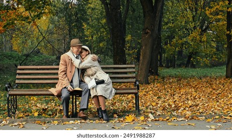 Elderly couple sitting reading a letter together on a bench in an autumn park then smiling and hugging each other - Powered by Shutterstock