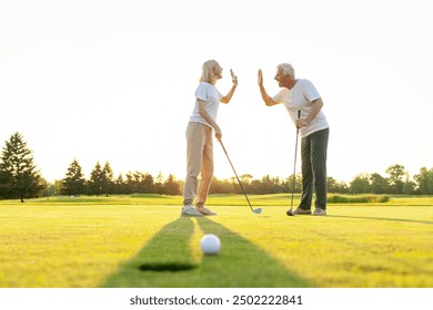 An elderly couple in sportswear exchange greetings on a golf course after a successful shot. Man and woman playing and succeeding together. Sunny day in the background  - Powered by Shutterstock