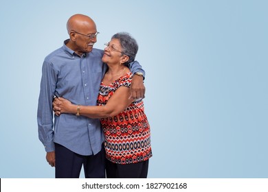 Elderly Couple Standing, Hugging And Looking At Each Other. Light Blue Gradient Background