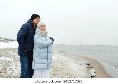 An elderly couple stands hugging on the beach by the sea in winter, looking into the distance. Holidays at sea. - Powered by Shutterstock