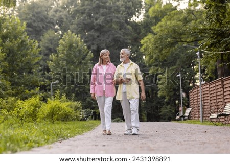 An elderly couple strolls hand in hand, exuding comfort and joy in a tranquil park, embodying lasting love and companionship.
