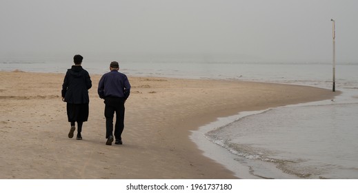 An elderly couple take a walk on a beach on a hazy morning. - Powered by Shutterstock