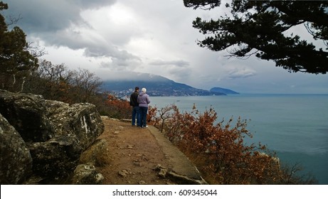 An Elderly Couple Takes A Walk Along The Black Sea Coast And Admire The Panoramic Views Towards The City Of Yalta