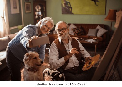 Elderly couple taking selfie while painting at home with their dog - Powered by Shutterstock