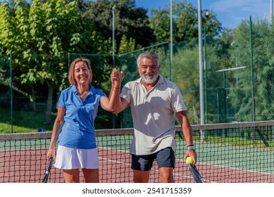 elderly couple of tennis players raises their hands in a victorious gesture while holding each other’s hands and smiling at the camera after winning their match - Powered by Shutterstock