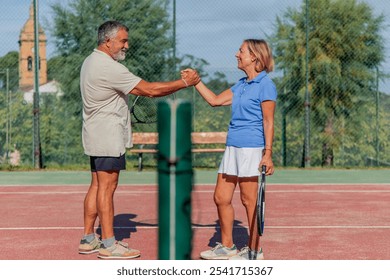 elderly couple of tennis players shares a joyful handshake, smiling at each other before the match begins. With the net in the front, this moment captures their friendship and enthusiasm for tennis - Powered by Shutterstock