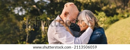 Elderly couple touching their heads together while standing outdoors. Happy senior couple sharing a romantic moment in a park. Cheerful mature couple expressing their love and affection.