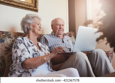 Elderly Couple Using Laptop Computer At Home. Senior Man And Woman Sitting On Sofa Working On Laptop.