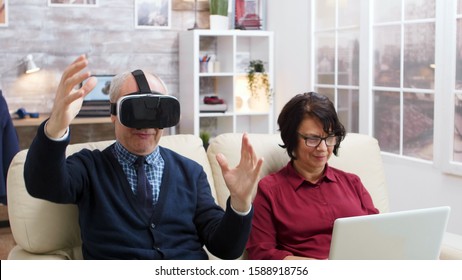 Elderly Couple Using Modern Technology To Watch Movies. Senior With Virtual Reality Goggles. Old Lady With Laptop.