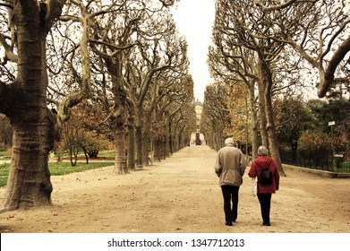 An elderly couple walking along the park in Paris, wondering on an alley between the high trees - Shutterstock ID 1347712013