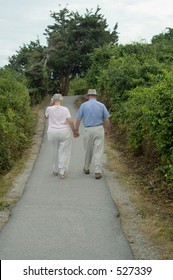 Elderly Couple Are Walking Away On The Walk Road.