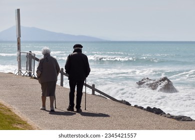 elderly couple walking on the promenade by the beach