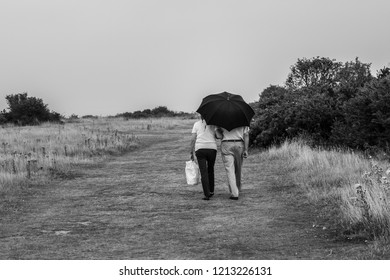 An Elderly Couple Walking Under An Umbrella In Walton On The Naze, Essex