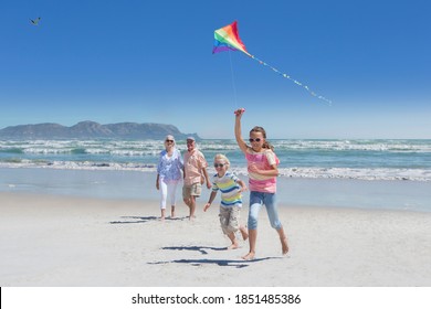 An elderly couple watching their grandchildren fly a kite on a sunny beach. - Powered by Shutterstock