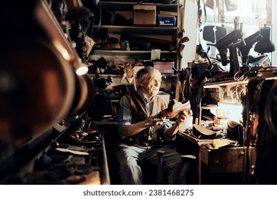 Elderly craftsman inspecting a handcrafted shoe in his traditional workshop - Powered by Shutterstock