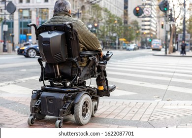An elderly disabled person on an electric wheelchair on a city street in front of a pedestrian crossing. The concept of modern technology for people with disabilities.