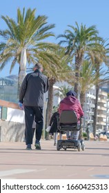 Elderly disabled person or senior on electric wheelchair or mobility scooter going with her husband. Elderly couple walking along a promenade on sunny day.  Modern technology for people disabilities