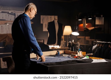 Elderly expert suitmaker alone in professional tailoring studio, designing upcoming fashion collection. Senior craftsman in atelier shop workspace manufacturing premium quality clothing - Powered by Shutterstock