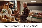 Elderly farmer in partnership with vendor bringing him boxes of fresh farm grown vegetables in local neighborhood grocery shop. Senior man supplying zero waste store with chemicals free produce