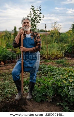 Elderly farmer posing for the camera after he is done digging with a shovel in his garden and smiling