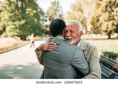 Elderly Father And Adult Son Hugging In The Park.