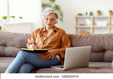 Elderly female in headphones and glasses writing in notebook and listening to music while sitting on couch near laptop
 - Powered by Shutterstock