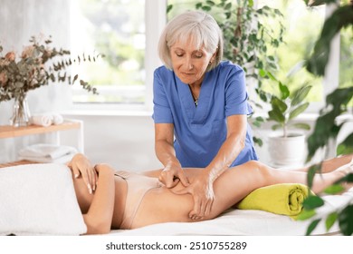 Elderly female masseuse in uniform doing thigh massage to young woman in spa salon - Powered by Shutterstock