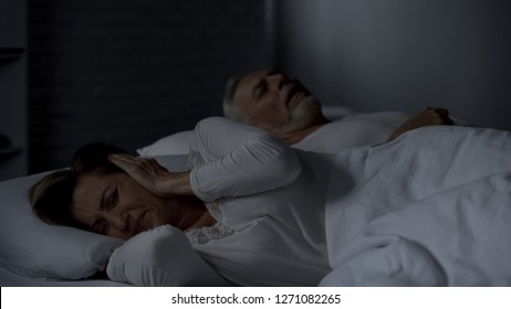 Elderly Female Pressing Hands Against Ears Cant Sleep, Man Snoring In Bed