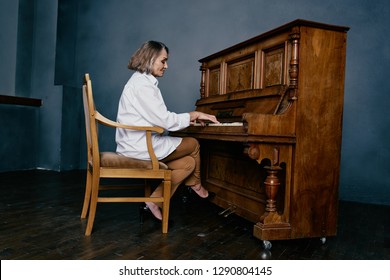 An elderly female teacher plays an ancient piano in a gray room         
