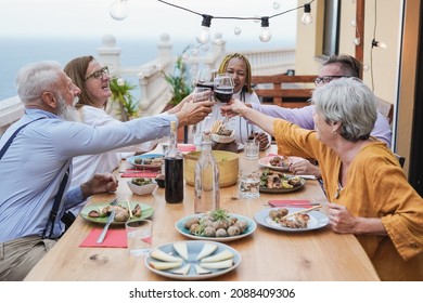 Elderly Friends Cheering At Dinner On Patio At Home - Multiracial Senior People Eating Together