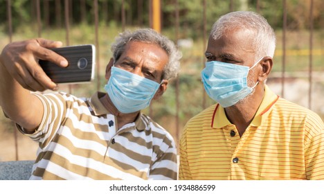 Elderly Friends With Medical Face Mask Taking Selfie While Sitting At Park - Concept Of Happy Senior People Friendship And Meetup After Lockdown Due To Coronavirus Covid-19 Pandemic