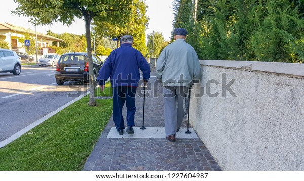 elderly\
gentlemen walking with the stick on the\
sidewalk