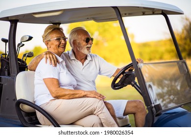 An elderly golf couple rides in a golf cart.