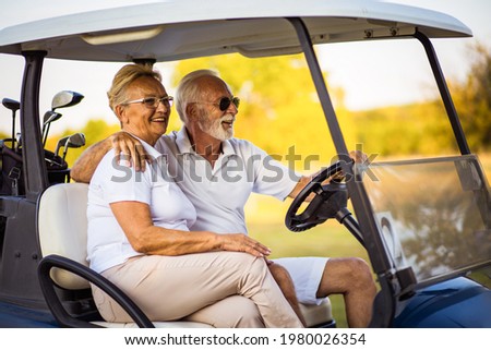 An elderly golf couple rides in a golf cart.