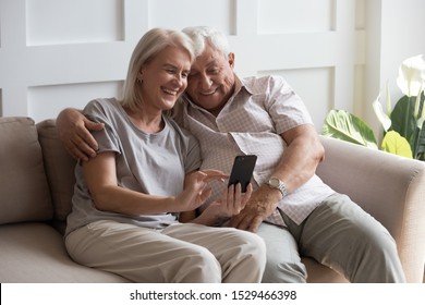 Elderly grandfather and grandmother spend time having fun using smartphone apps, middle-aged wife enjoy online entertainments, taking selfie with old husband, older generation and modern tech concept