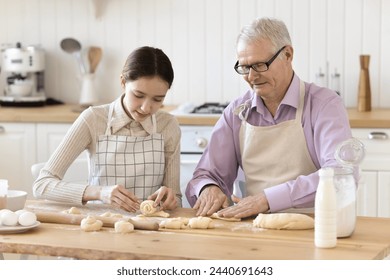 Elderly grandfather teaching pre-teen granddaughter to cook, multi generational relatives wear aprons cooking, talking preparing homemade dough for sweets in modern kitchen. Culinary, family recipe - Powered by Shutterstock