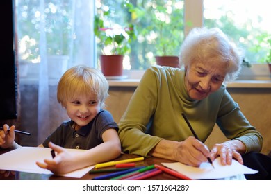 Elderly Grandmother Helping Little Grandchild Doing Homework. Grandma And Grandson Drawing Together. Quality Family Time.