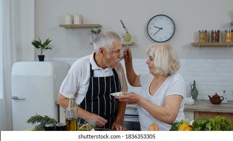 Elderly Grandparents In Modern Kitchen Interior. Senior Woman Feeding Man With Raw Sprouts Buckwheat With Nuts. Eco Food Eating Diet. Healthy Mature Family Lifestyle. World Vegan Day