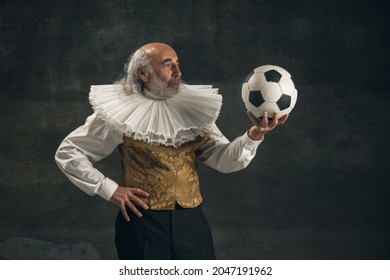 Elderly gray-haired man posing with football ball isolated on dark vintage background. Retro style, comparison of eras concept. Old male model like sad actor, clown .