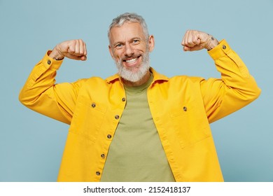 Elderly Gray-haired Mustache Bearded Man 50s In Yellow Shirt Showing Biceps Muscles On Hand Demonstrating Strength Power Isolated On Plain Pastel Light Blue Background Studio People Lifestyle Concept