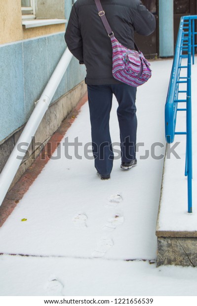 An elderly\
gray-haired sick man climbs hard on a snow-covered ramp for the\
disabled, leaving traces in the\
snow