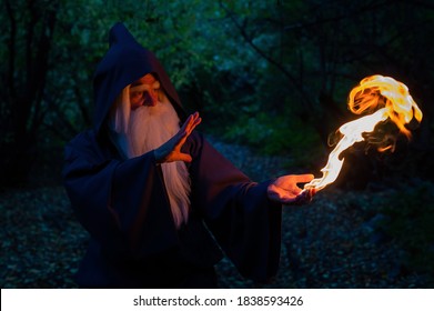 An elderly gray-haired witcher casts a fire spell in the forest. Man in wizard costume