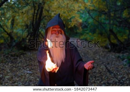An elderly gray-haired witcher casts a fire spell in the forest. Man in wizard costume