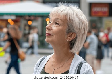 An elderly gray-haired woman aged 65-70 looks up at a blurred urban background. - Powered by Shutterstock