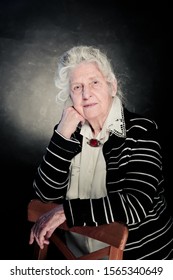 Elderly Gray-haired Woman Dressed In A White Blouse With Embroidery And An Amber Vintage Brooch. She Looks Like A Professor, Doctor Or Scientist. Dignity, Confidence, Wisdom