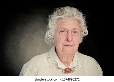 Elderly Gray-haired Woman Dressed In A White Blouse With Embroidery And An Amber Vintage Brooch. She Looks Like A Professor, Doctor Or Scientist. Dignity, Confidence, Wisdom